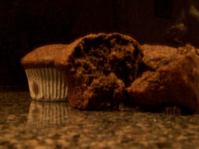 Close-up of three chocolate muffins, one with a bite taken out, on a shiny counter.