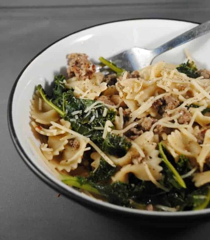 White bowl with italian sausage, farfalla pasta and kale