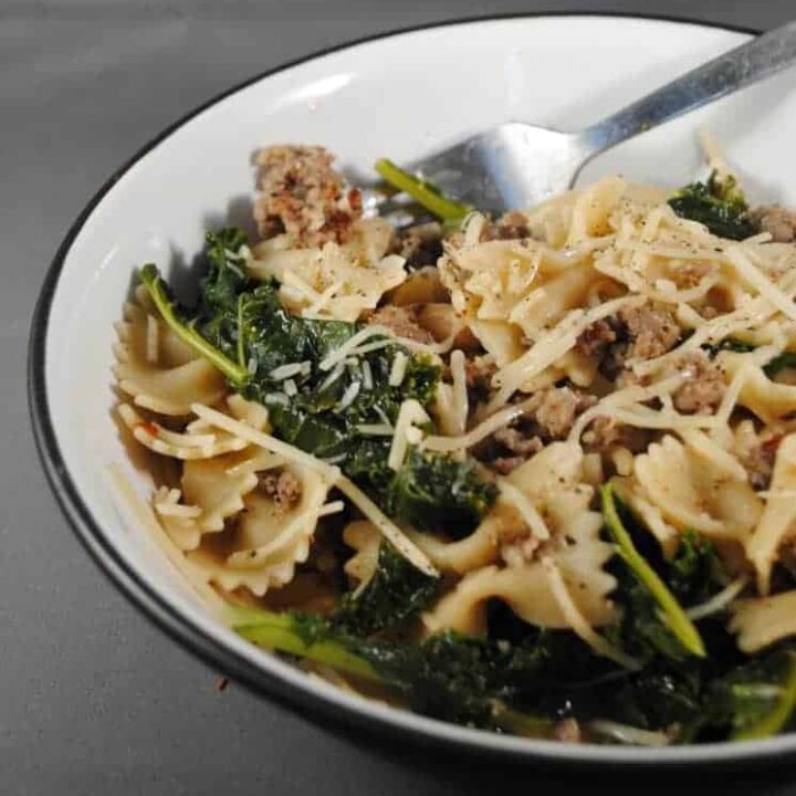 White bowl with italian sausage, farfalla pasta and kale