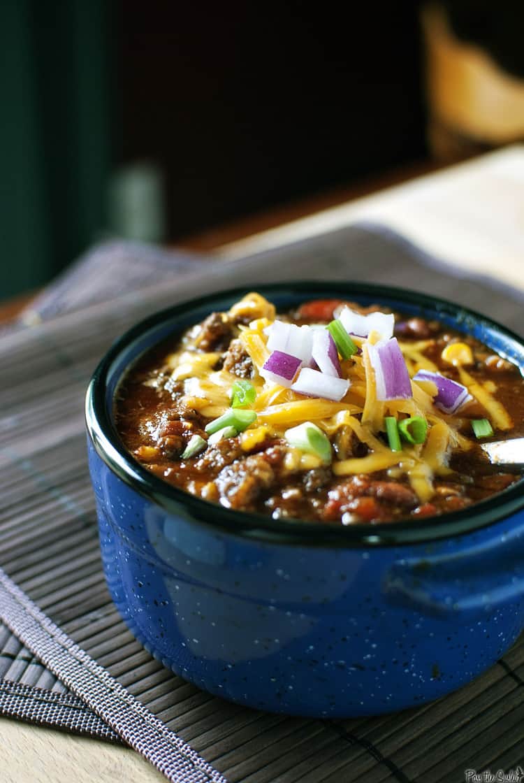 Bowl of crock pot chili with cheese, onions, and scallions on top.