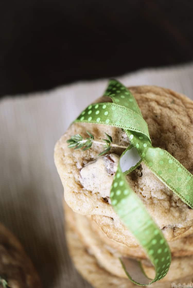 Chewy chocolate chip cookies stacked with thyme sprigs and a ribbon.