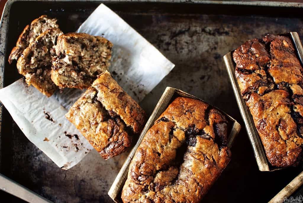 showing 3 loaves of nutella swirled banana bread with one sliced from above on black board