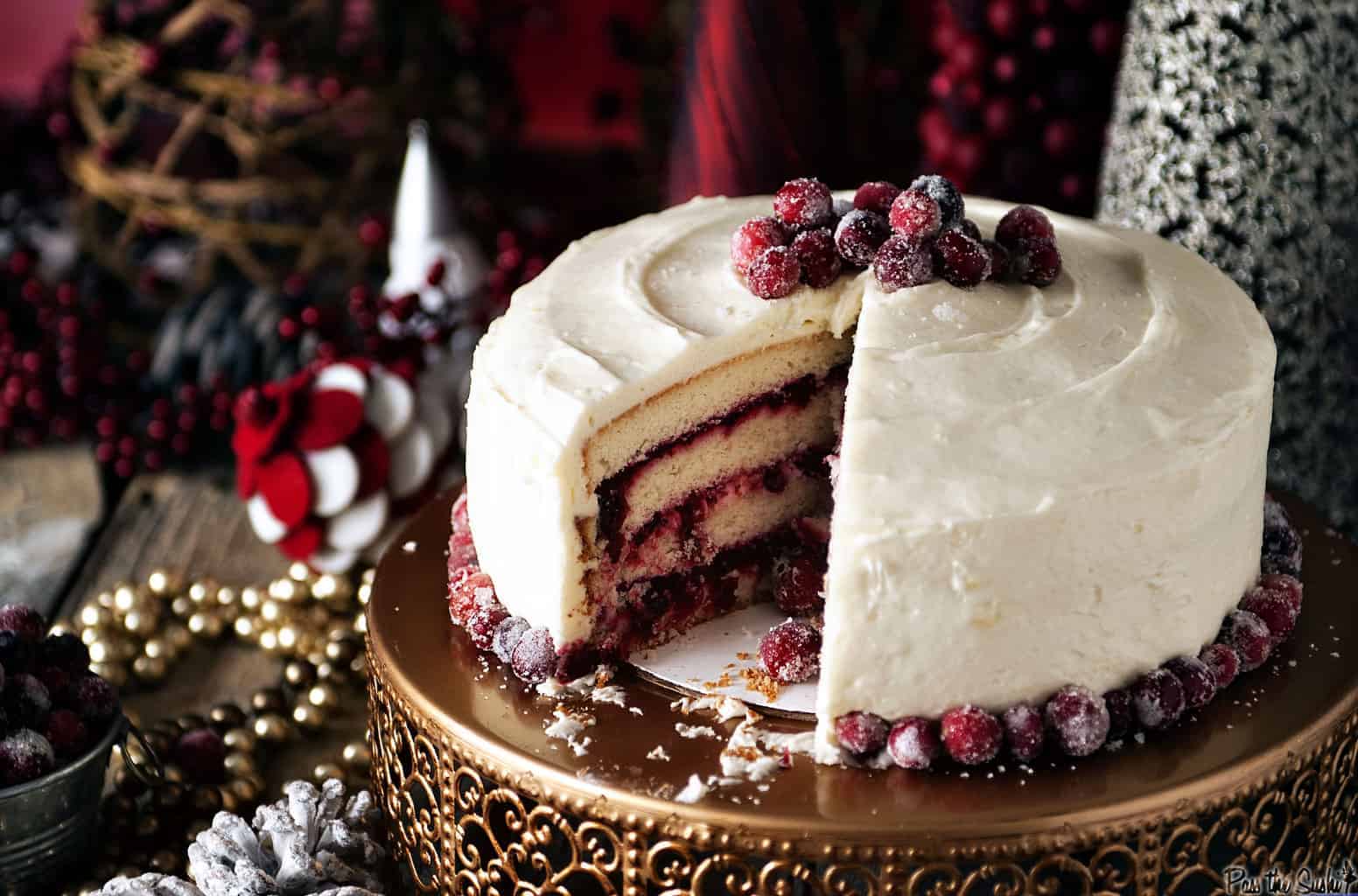 A beautiful red and white striped cranberry cake with a slice taken out to show the layers of cake and red filling.