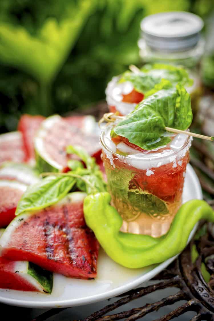 Cocktail glass filled with spicy margarita on a platter of grilled watermelon.