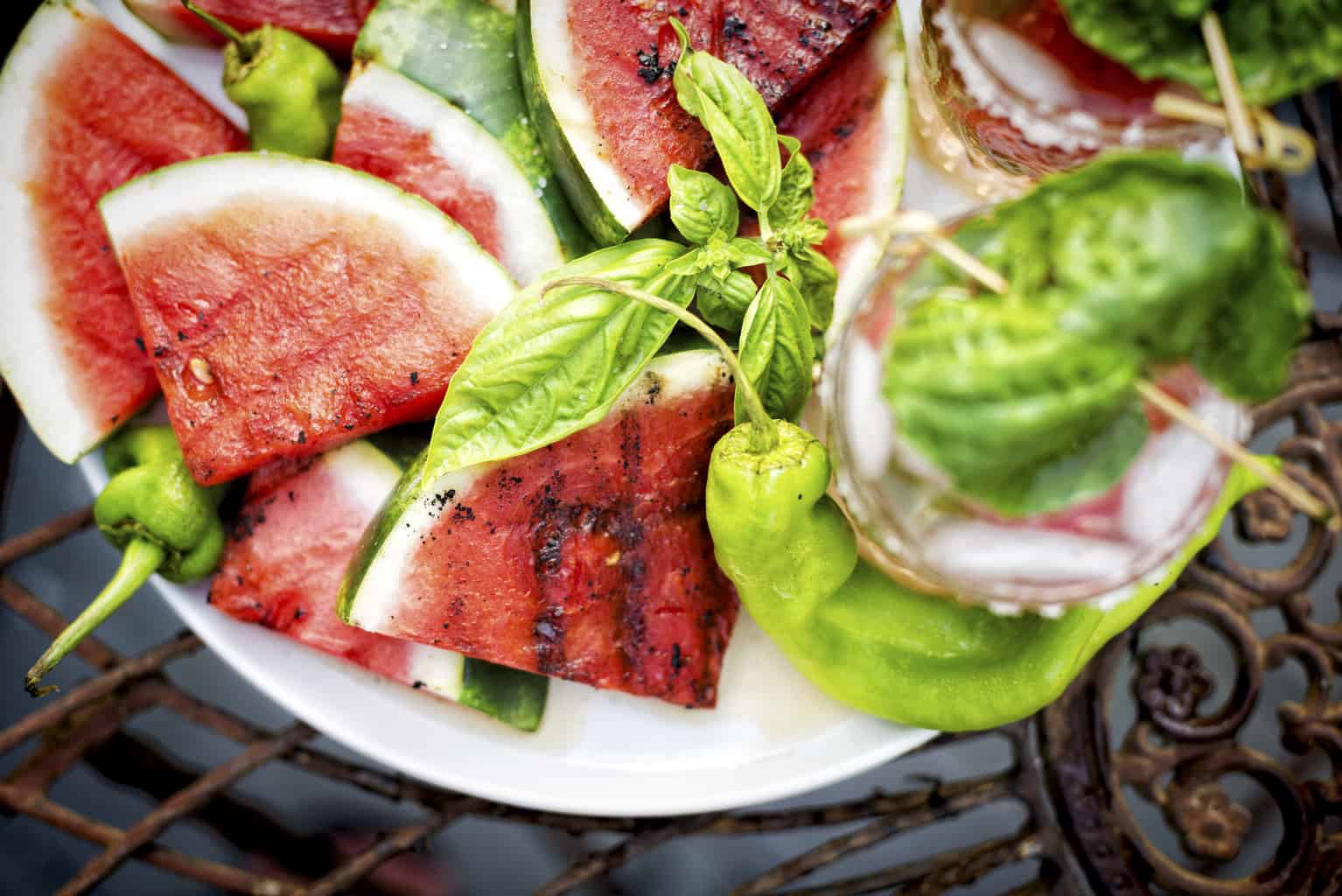 Overhead shot of grilled watermelon with soft focus cocktails. 