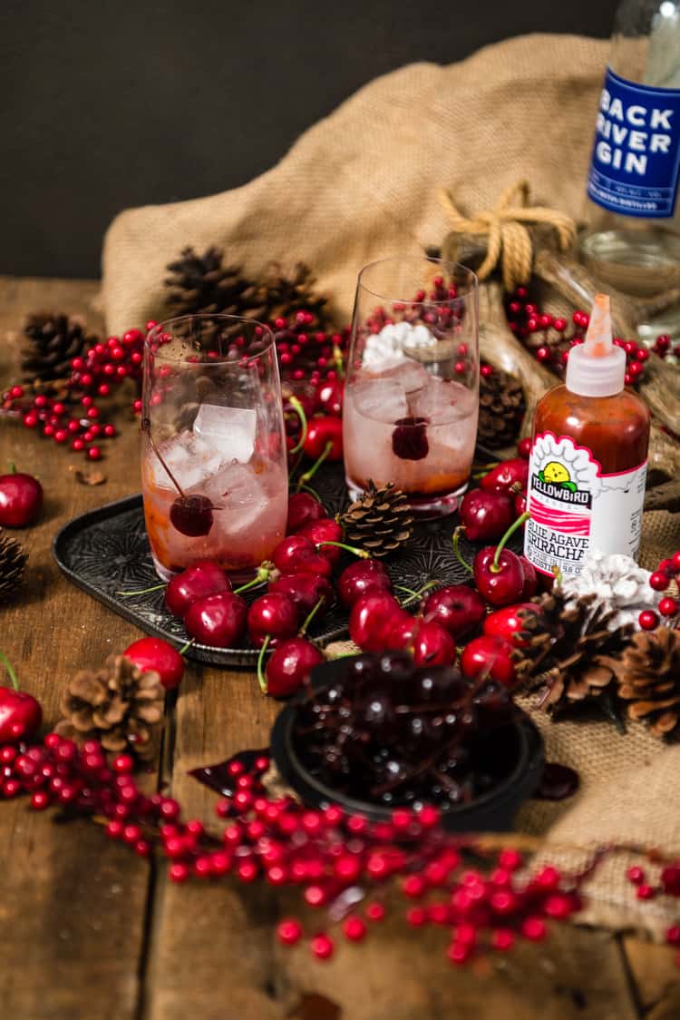 Two highball glasses with rocks, cherries and the beginnings of a good cocktail. 