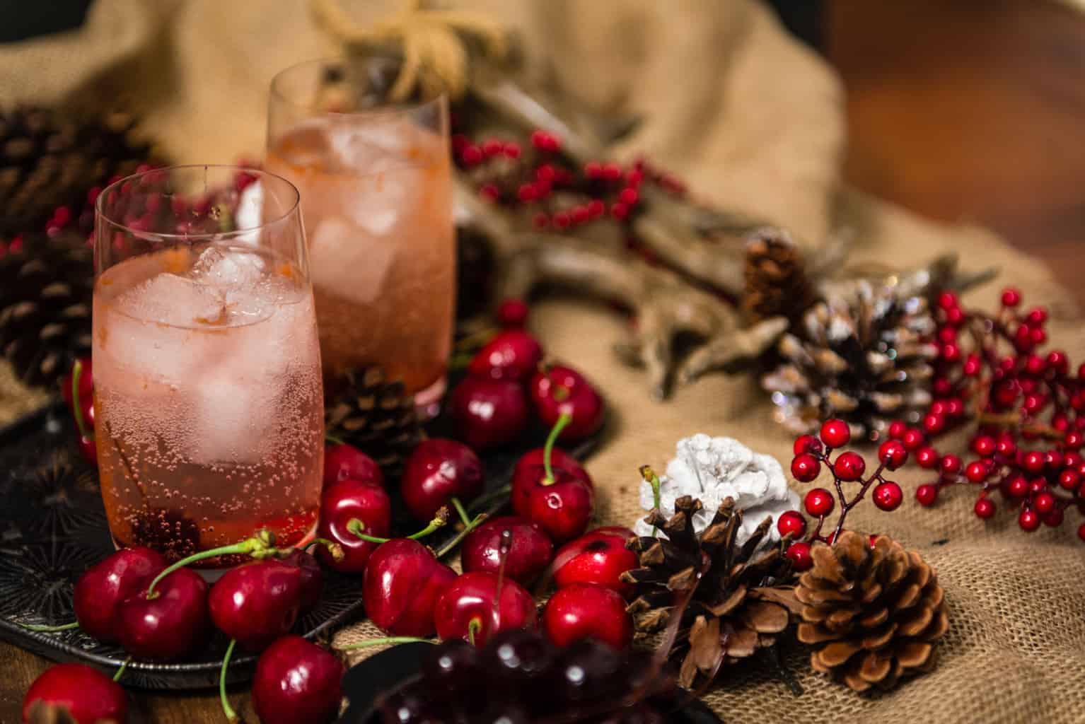 Dirty Shirley in a highball glass on ice with fresh cherries in the foreground. 