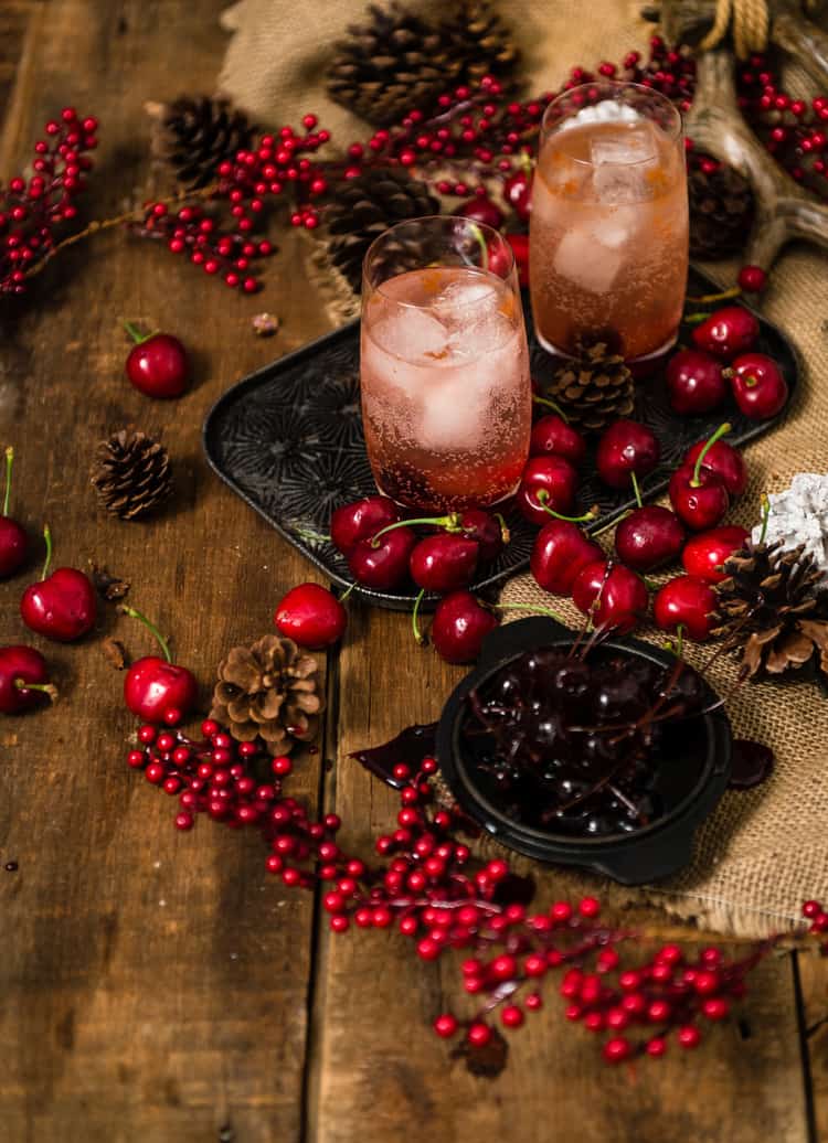 Pink bubbling drinks in highball glasses surrounded by cherries. 