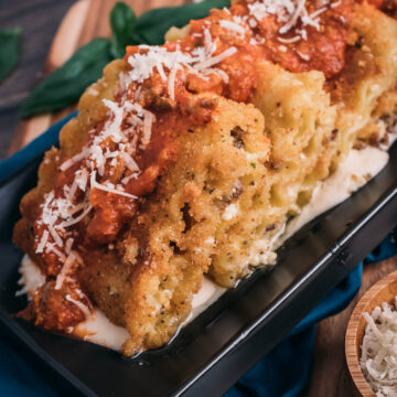 platter of fried lasagne fritta, with alfredo on a black plate, lasagna roll ups and topped with marinara and parmesan.