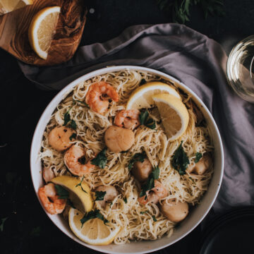 above shot of shrimp and scallop scampi over angel hair pasta with lemon wedges on table