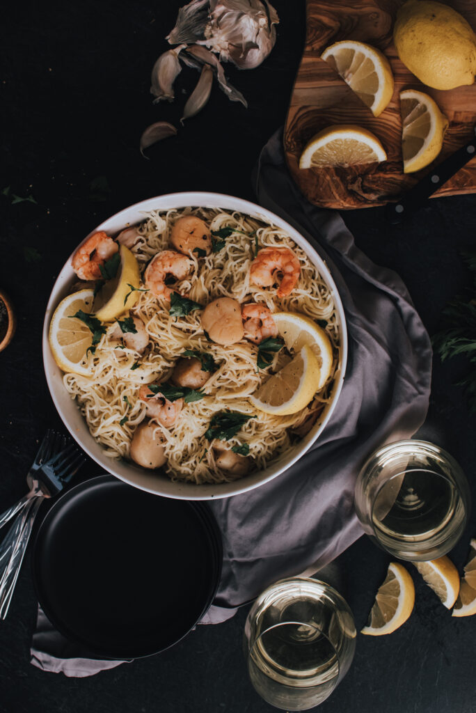 above shot of shrimp and scallop scampi over angel hair pasta, wine glasses, lemon wedges on table