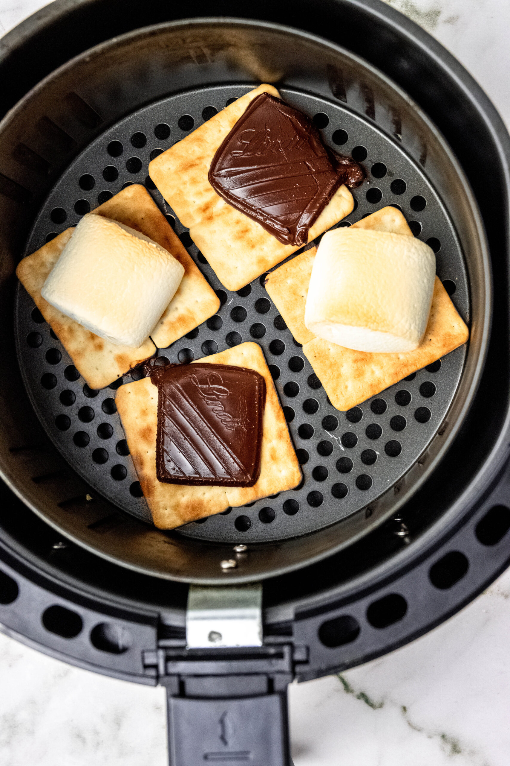 Overhead of air fryer basket with smores ingredients.