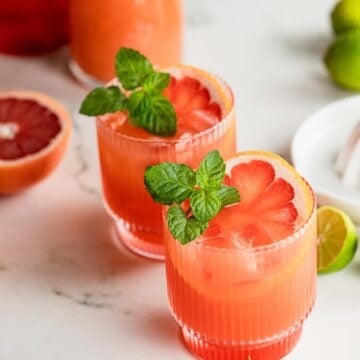 Angled shot of cocktail glasses filled with bright red cocktail and garnished with mint sprigs.