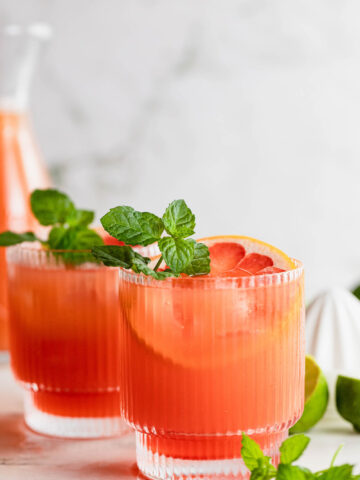 Side shot of cocktail glasses filled with this drink and garnished with mint and grapefruit.