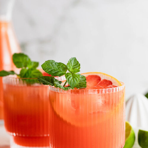 Side shot of cocktail glasses filled with this drink and garnished with mint and grapefruit.