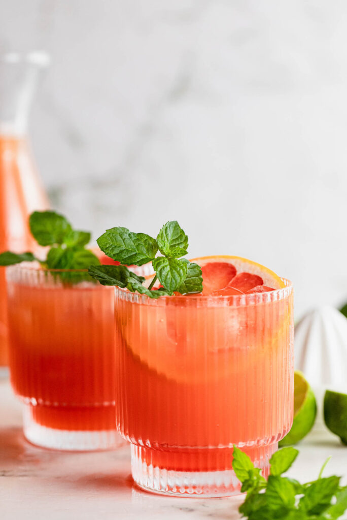 Side shot of cocktail glasses filled with this drink and garnished with mint and grapefruit.