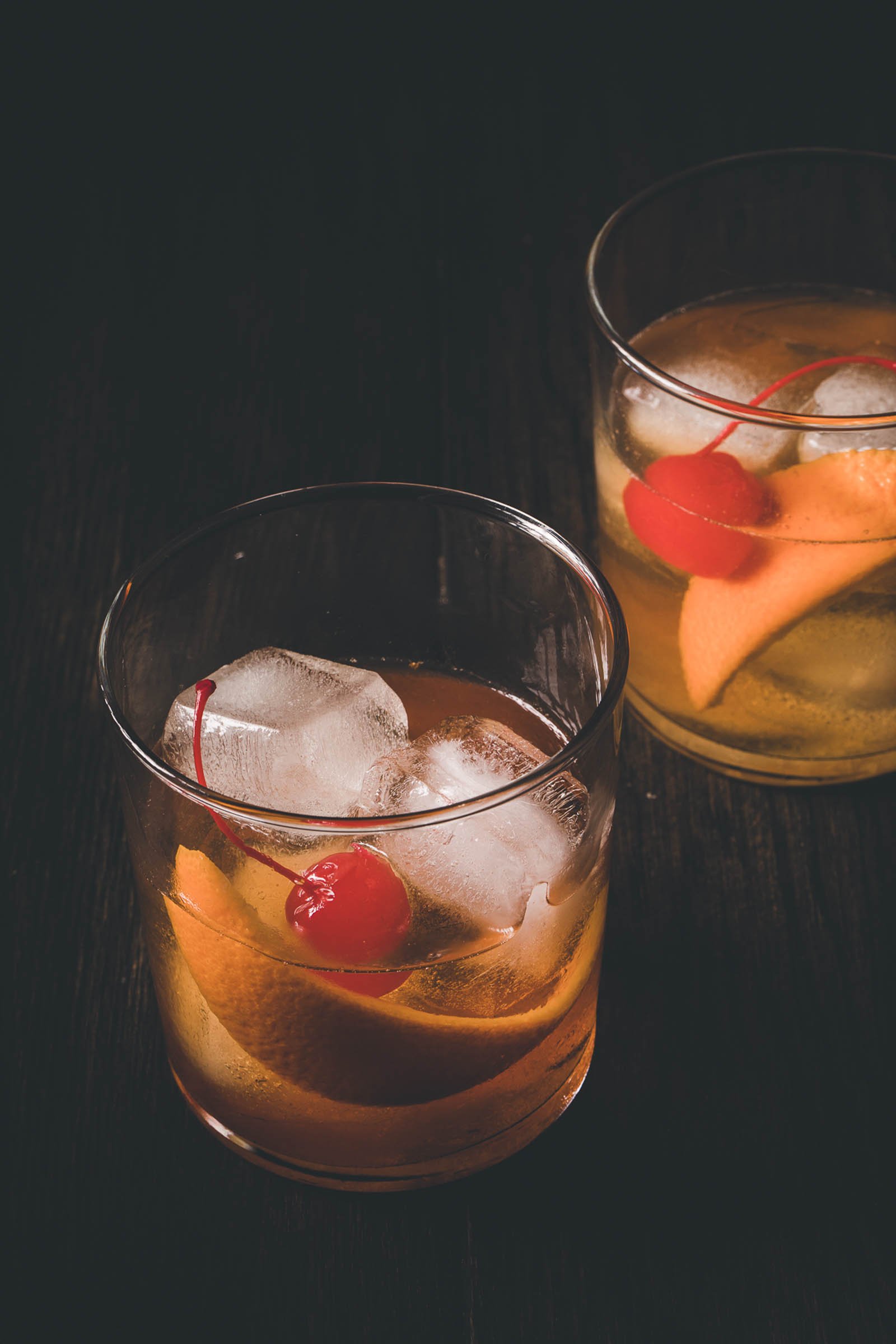 Smoked old fashioned cocktails in highball glasses with orange peel and cherry. 