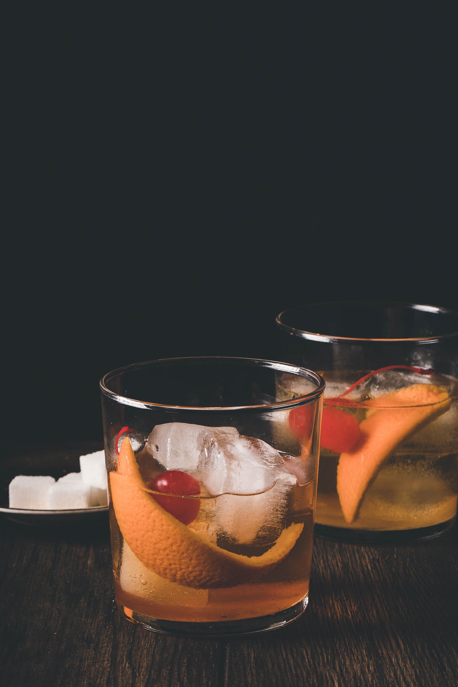 Highball glasses filled with old fashions and sugar cubes in the background.