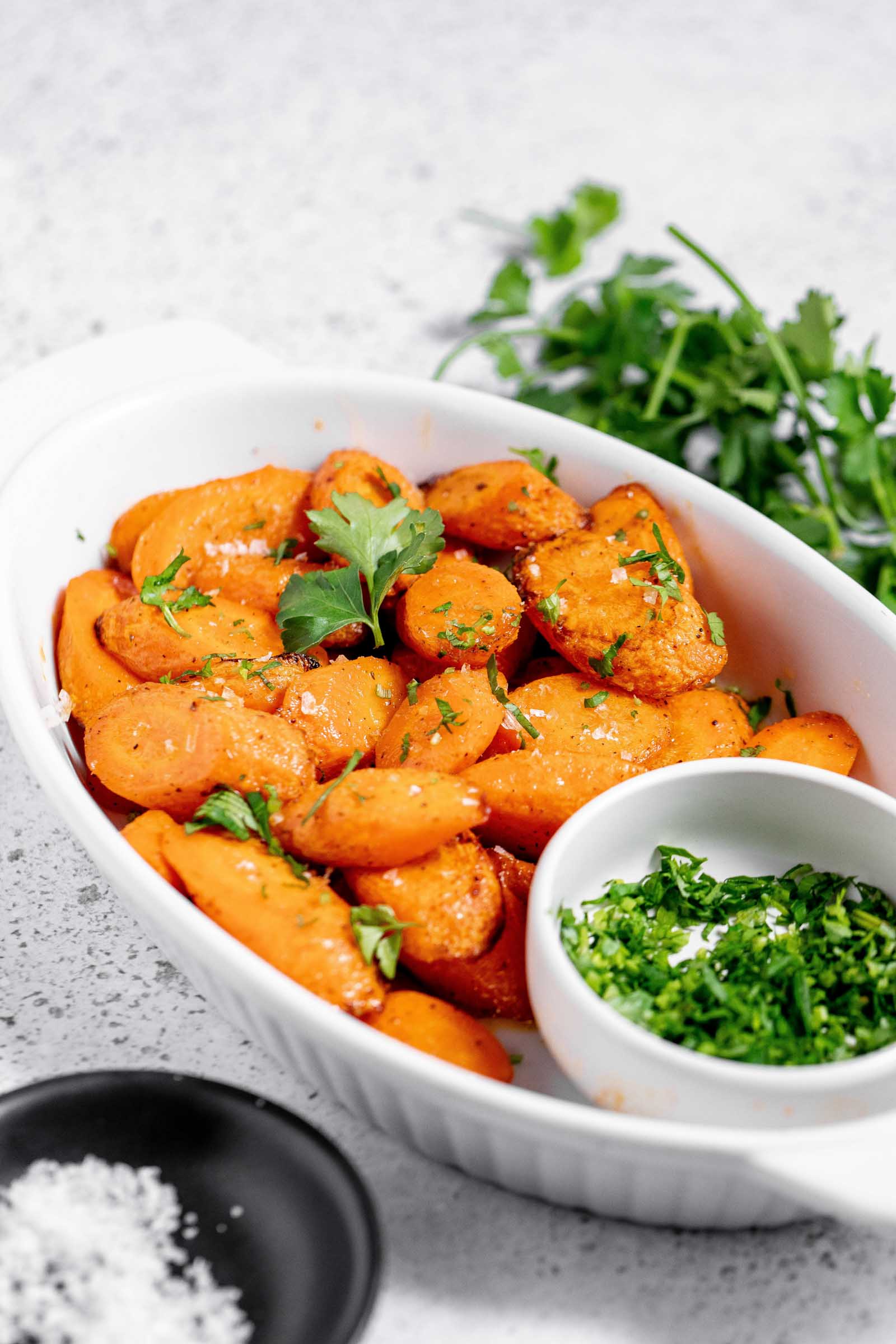 White dish filled with crisp cooked carrots garnished with herbs and salt. 
