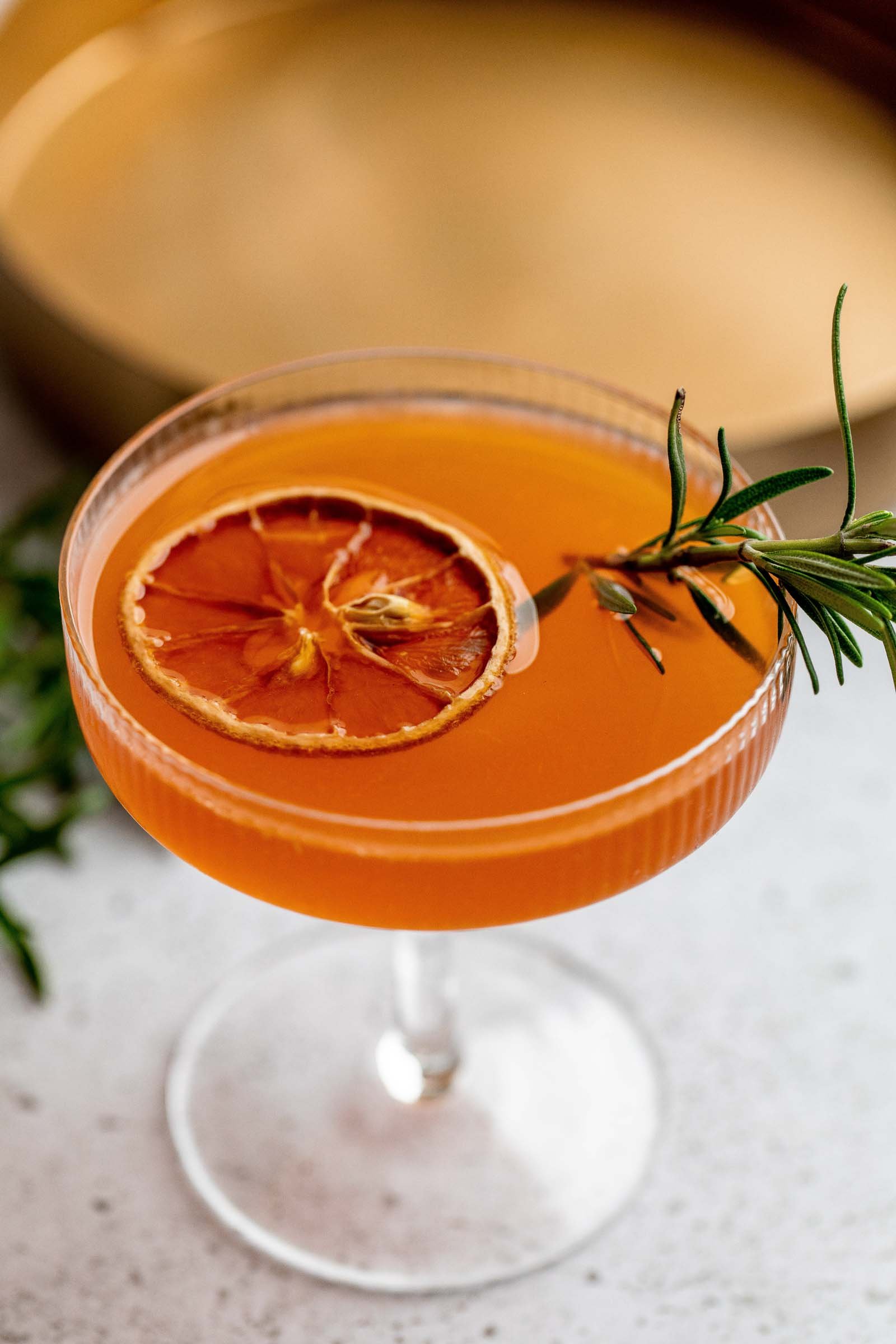 Close up of gold rush cocktail with orange slice and rosemary garnish.