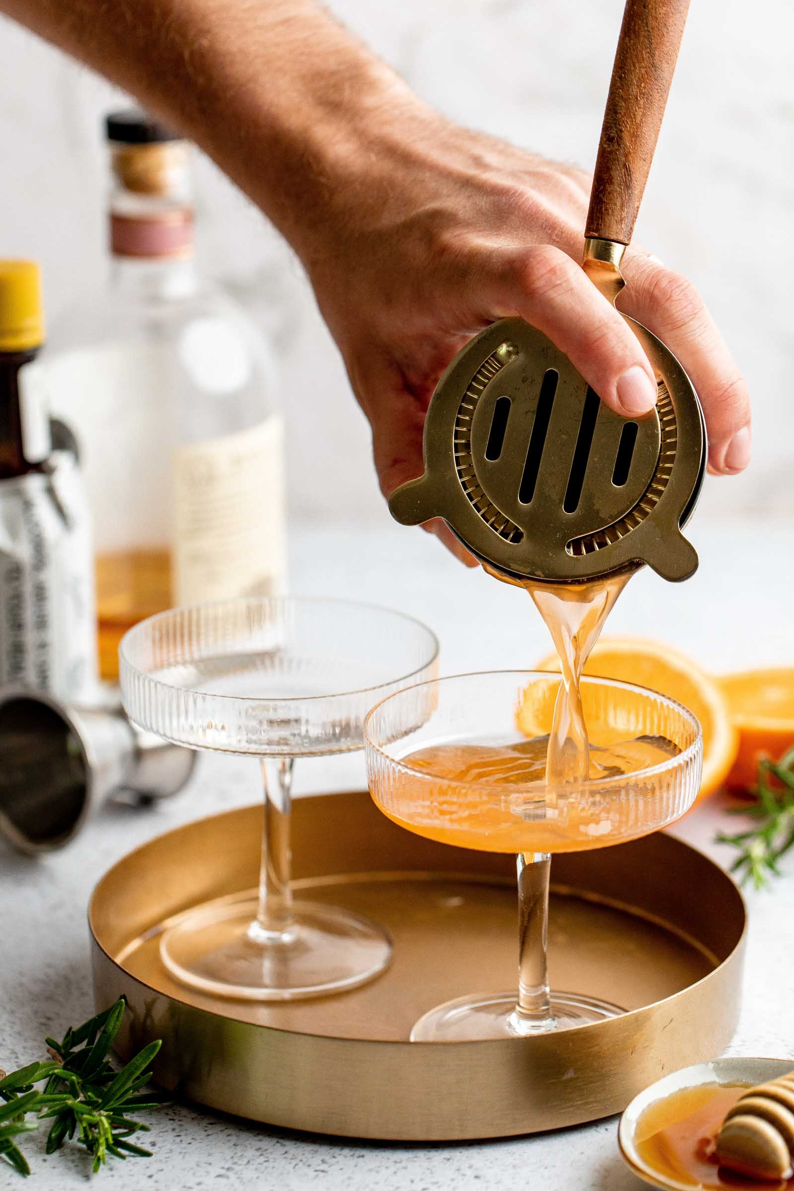Hand straining cocktail into glass with cocktail strainer.