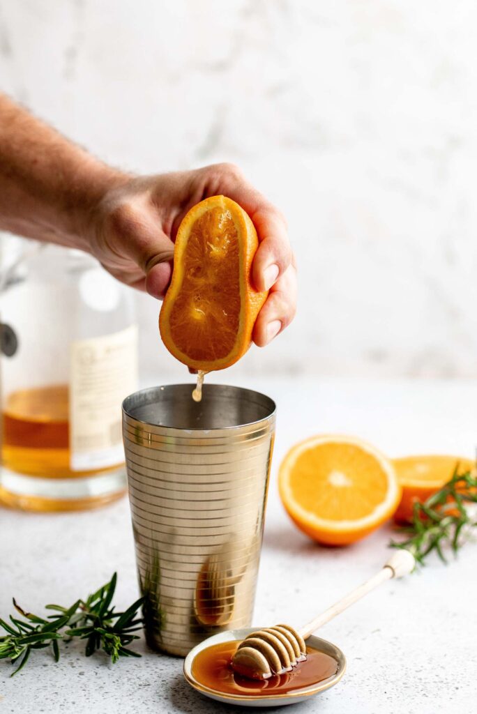 Hand squeezing orange juice into cocktail mixer.