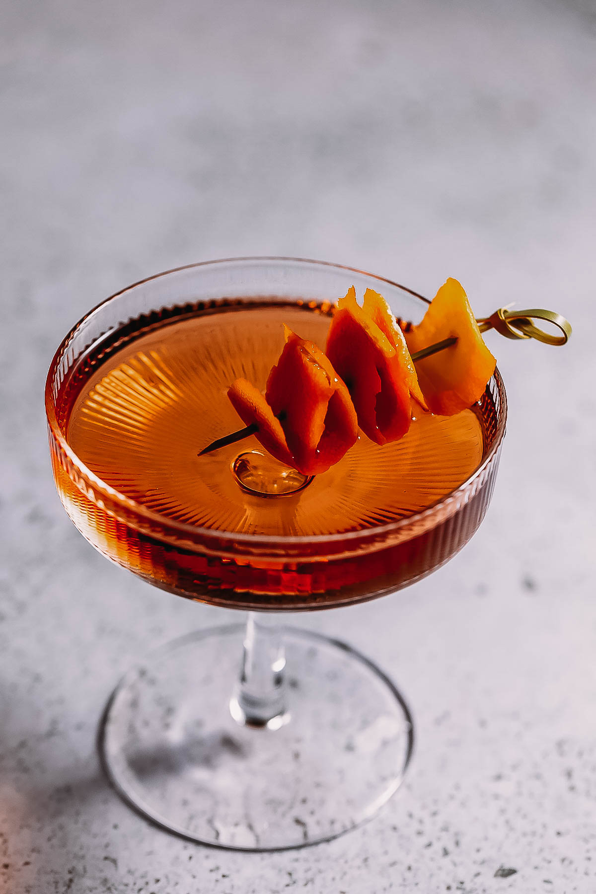 Overhead image of a coupe glass filled with a brandy manhattan and garnished with citrus.