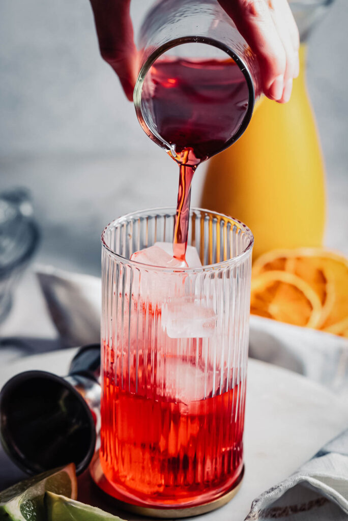 Cranberry juice being poured from a jigger. 