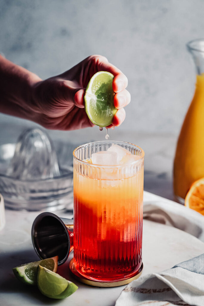 Hand squeezing lime juice into cocktail. 