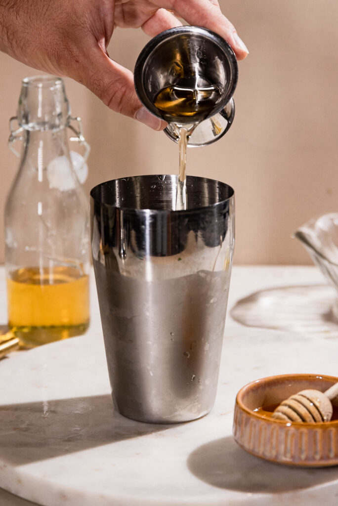 Honey syrup being poured into a cocktail shaker. 