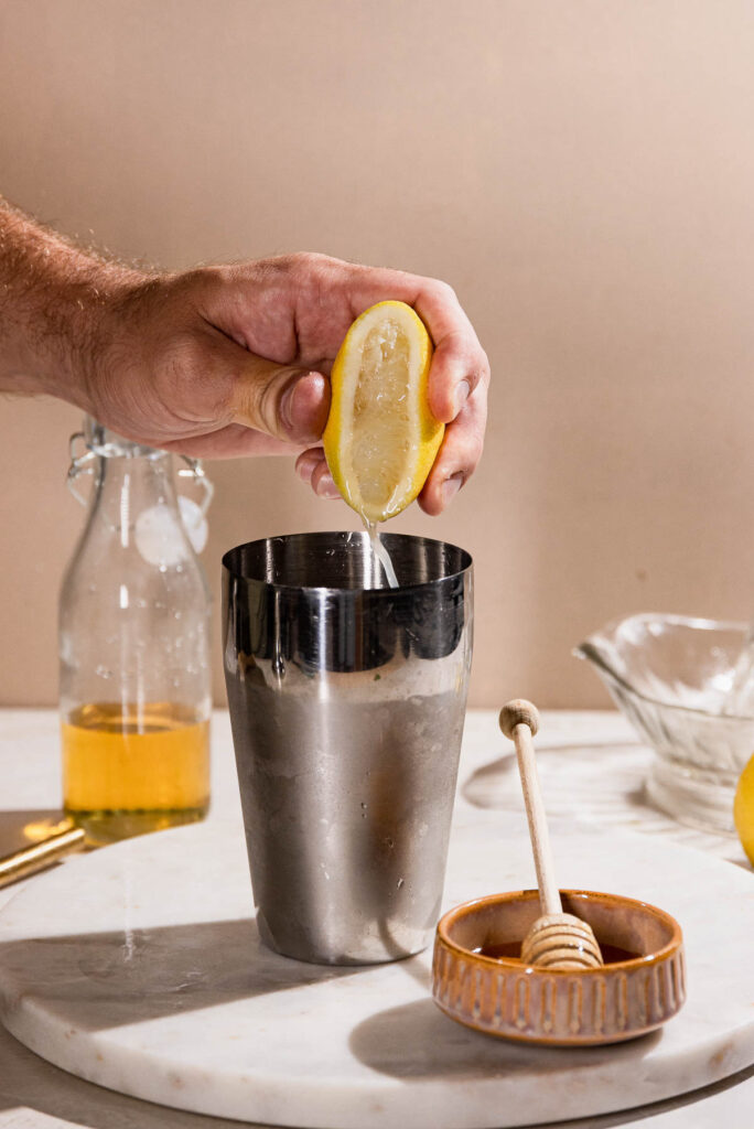 Lemon being squeezed into cocktail shaker. 