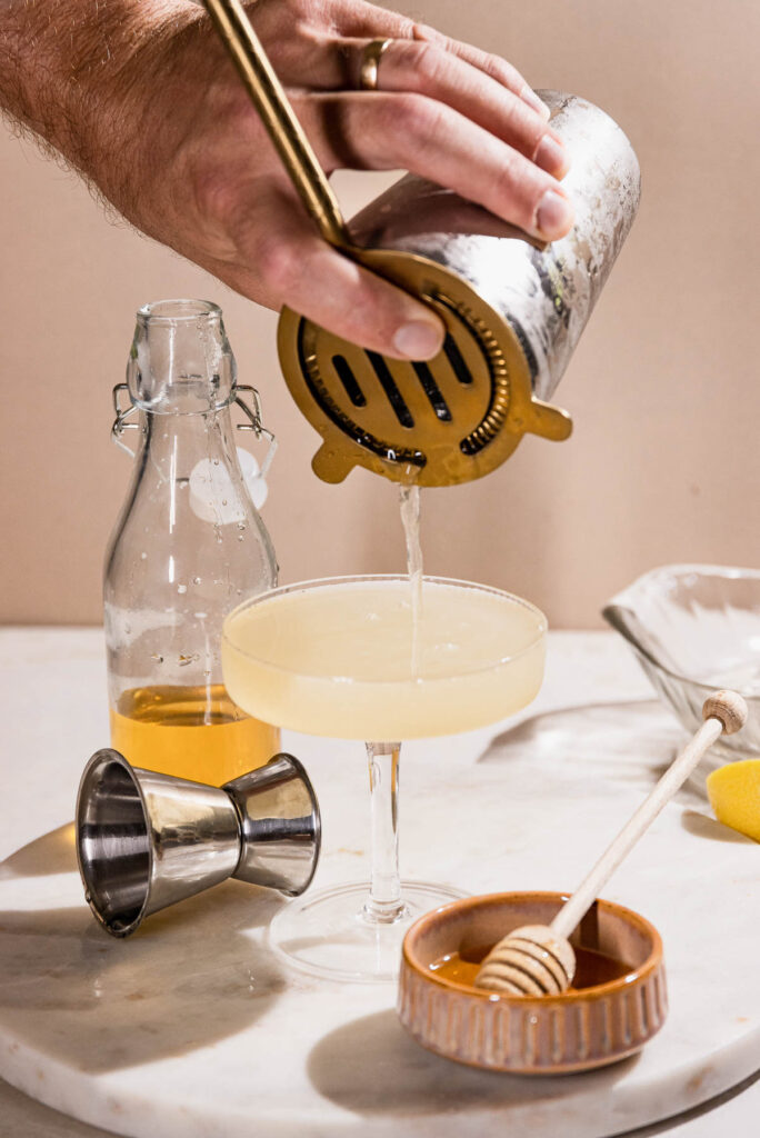 Cocktail being strained into coupe glass. 