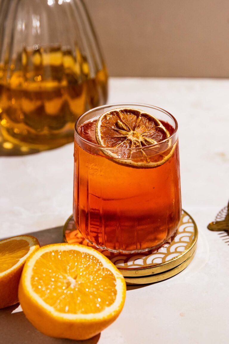 Side shot of a rimmed rocks glass with a orange toned Boulevardier cocktail in the center.