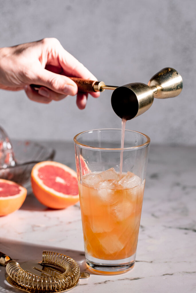 Adding grapefruit juice to a cocktail shaker. 