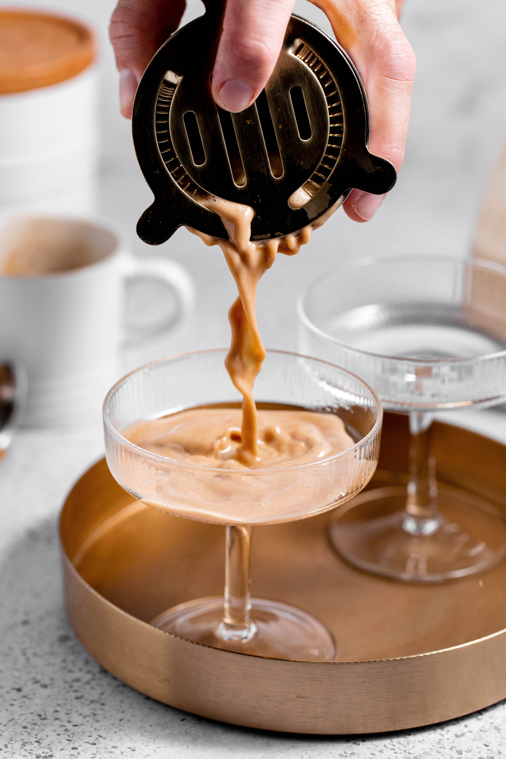 Hand straining espresso martini into a glass. 