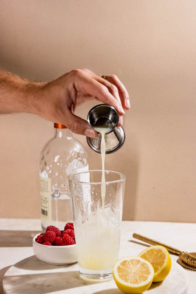 Hand pouring lemon juice into a cocktail.