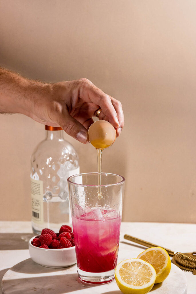 Hand cracking egg white into a cocktail shaker. 