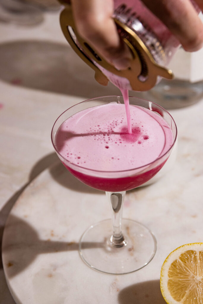 Straining the frothy pink cocktail into a coupe class. 