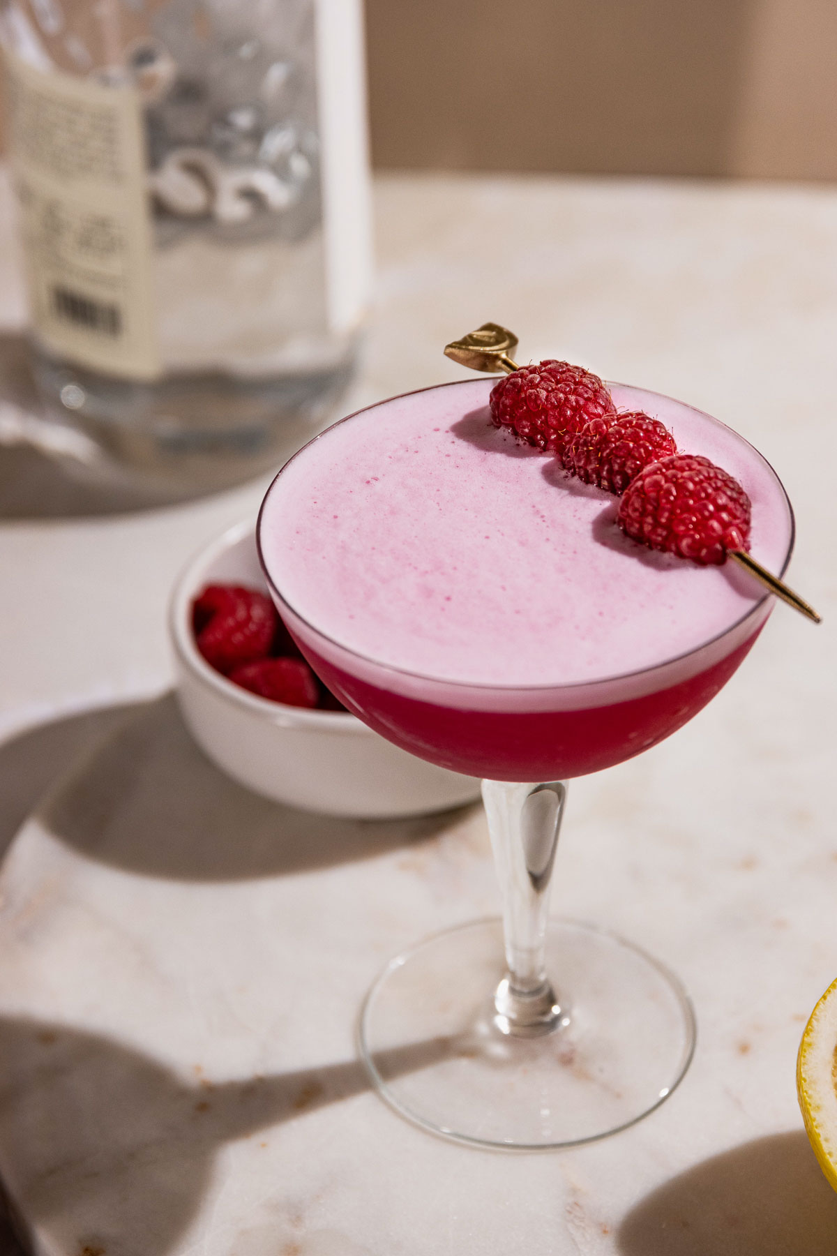 Close up of clover club cocktail showing raspberries on a cocktail pick. 