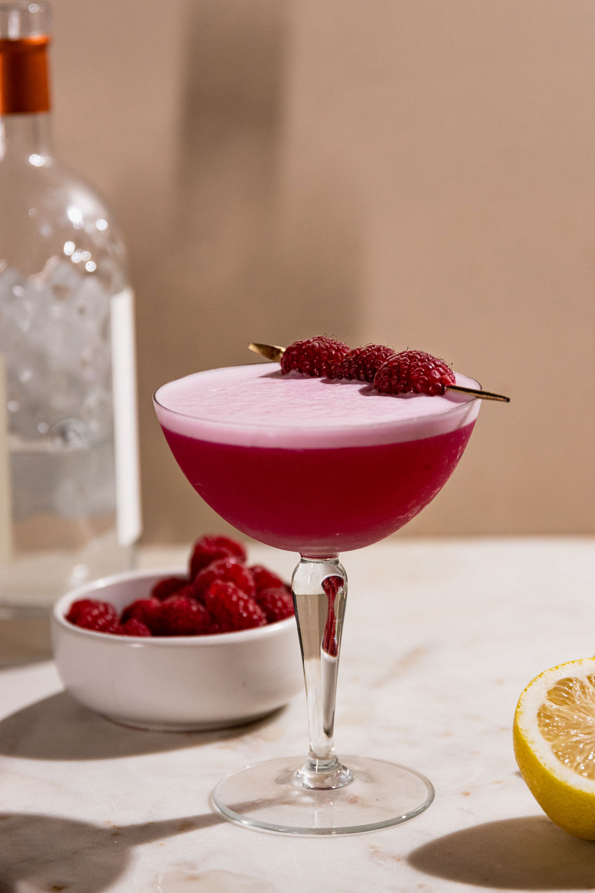 Side shot of pink cocktail garnished with raspberries. 