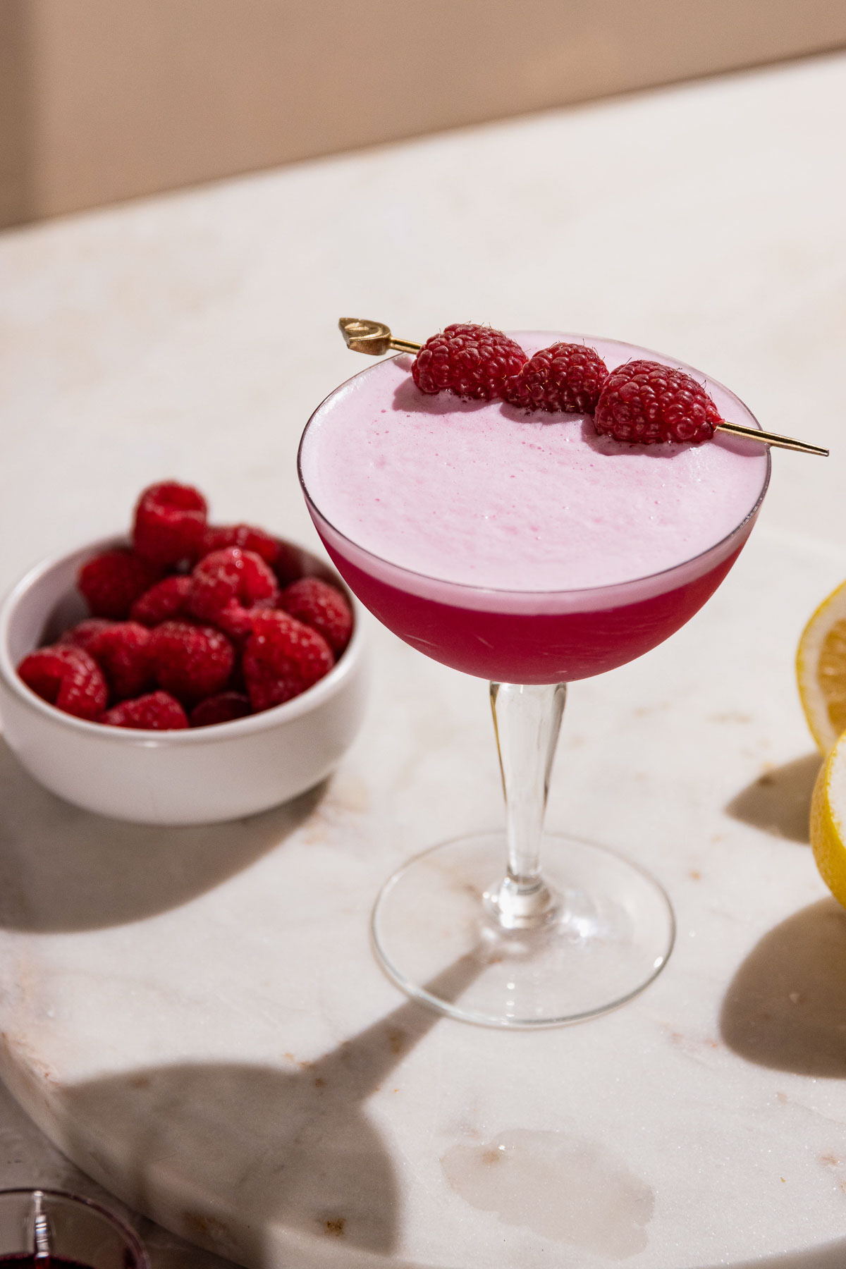 Frothy pink clover club cocktail on a table with raspberries and lemons. 