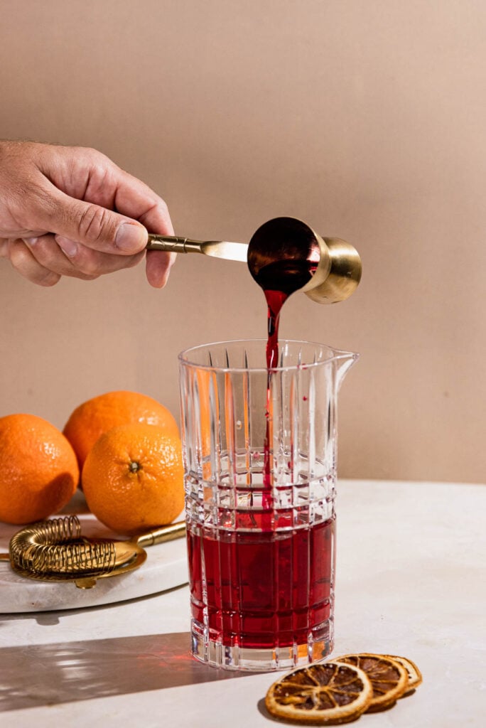 Grenadine poured from a jigger into a cocktail shaker. 