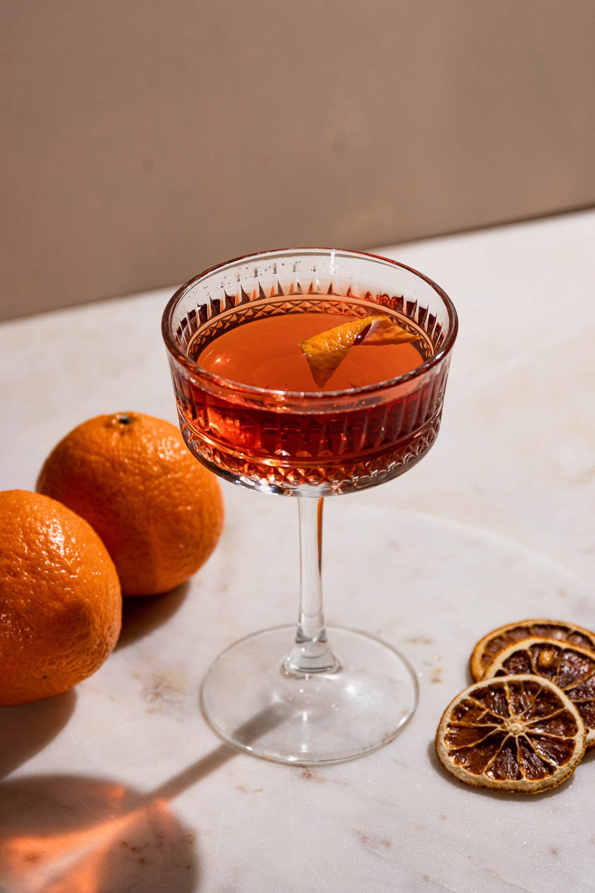 Dried orange slices, fresh oranges, and an orange peel as garnish in an el presidente cocktail in a coupe glass. 