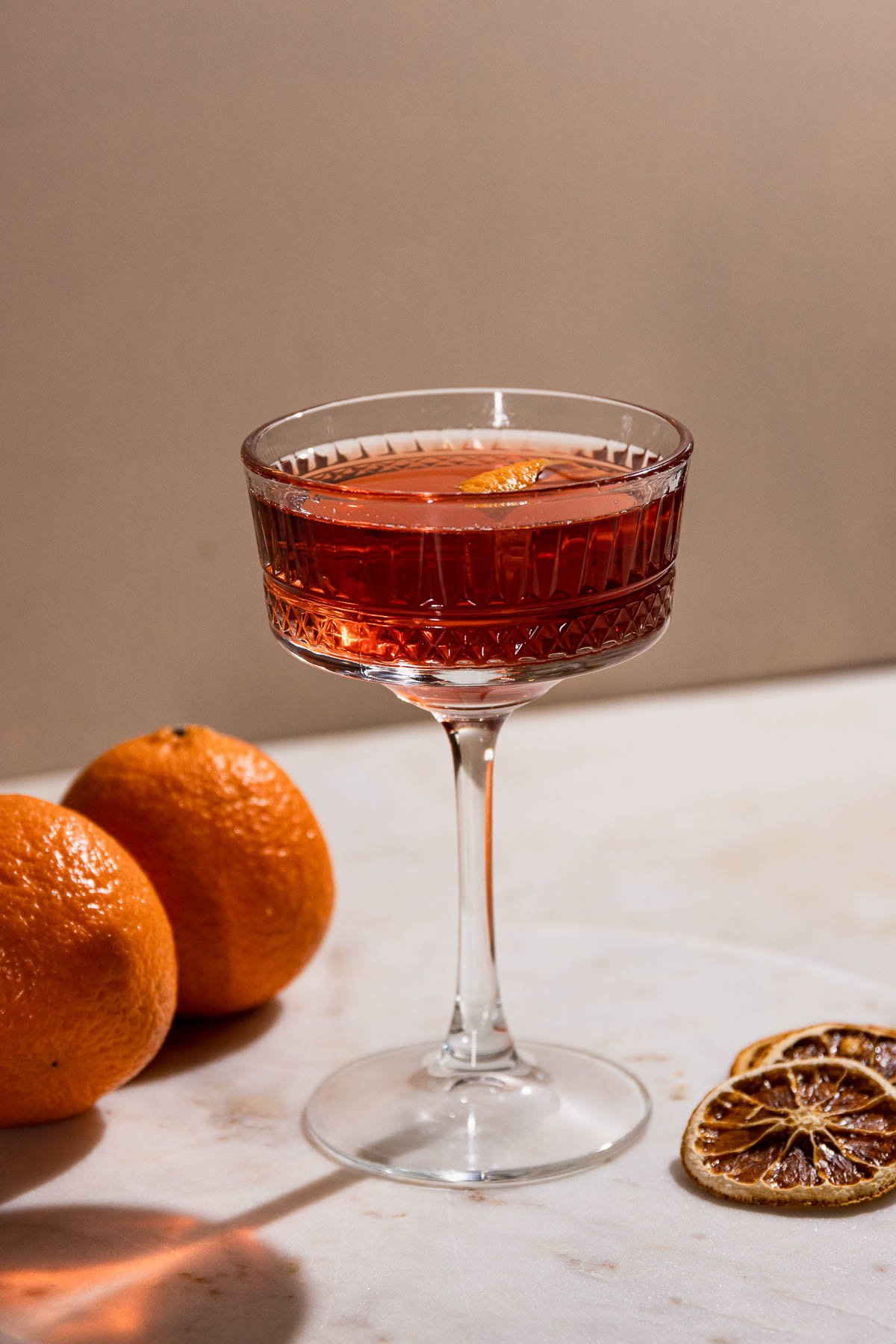 Side shot of a beautiful coupe glass filled with a dark orange cocktail. 