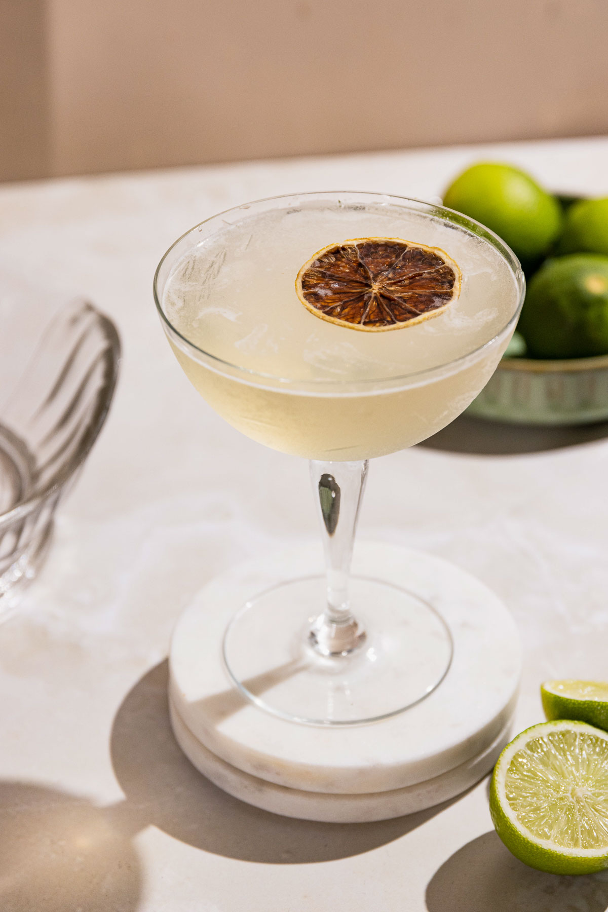 Frosty gimlet cocktail in a coupe glass on a table with fresh limes. 