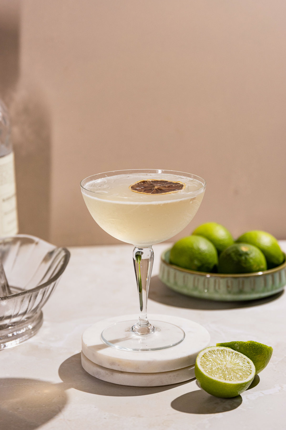 Side shot of a coupe glass filled with a gimlet cocktail and a lime slice. 