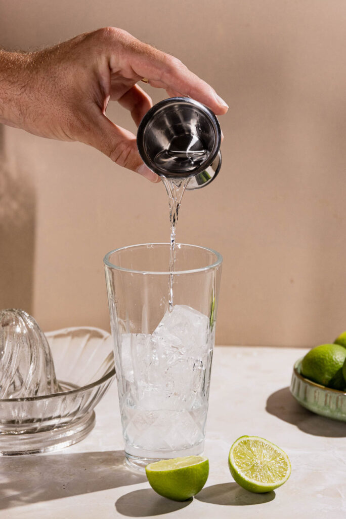 Hand pouring gin into a cocktail shaker. 