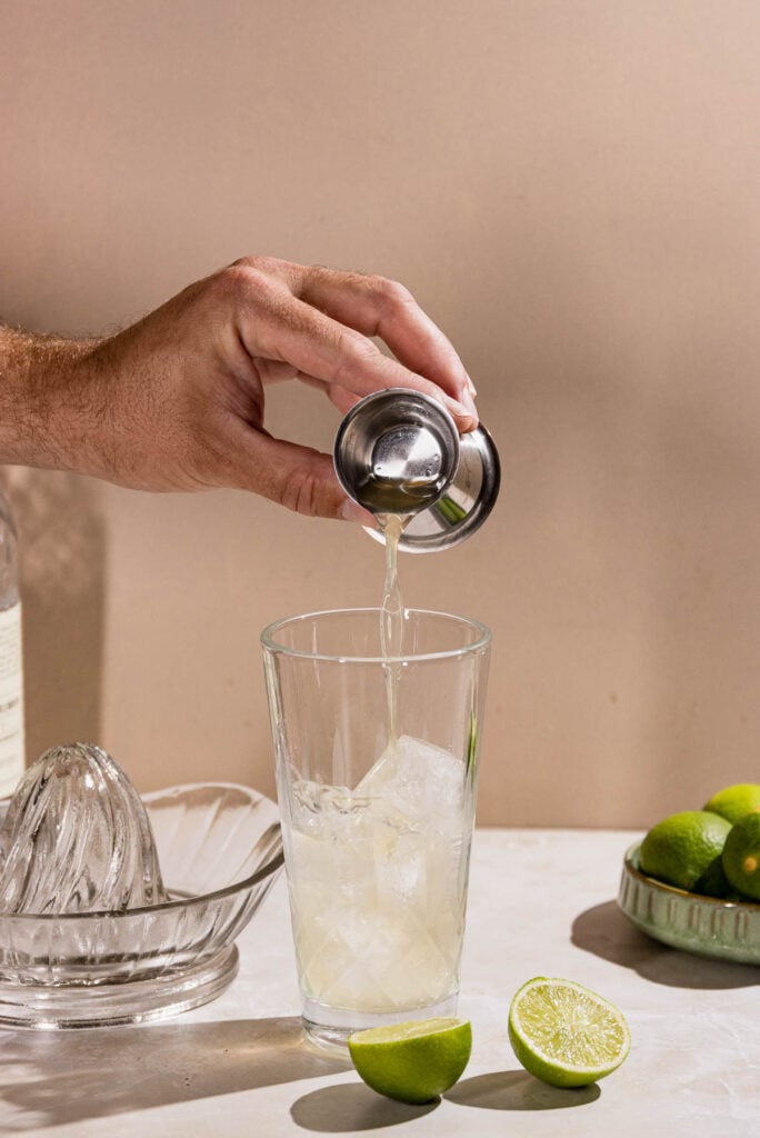 Hand pouring lime juice into a cocktail shaker. 