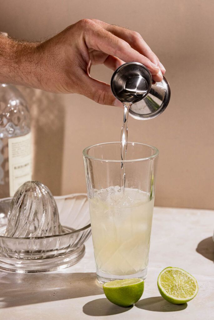 Hand pouring simple syrup into a cocktail shaker. 