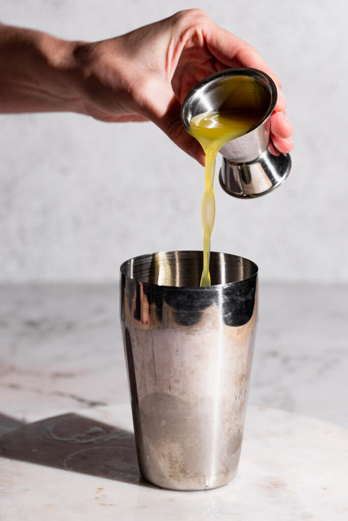 Hand pouring pineapple juice into a cocktail shaker.